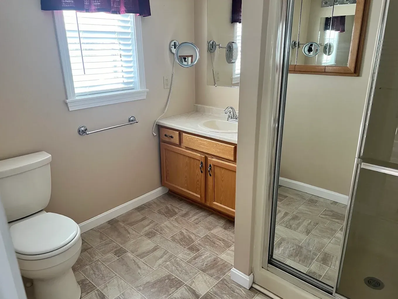 Small beige bathroom with toilet, vanity sink, window, and glass shower door
