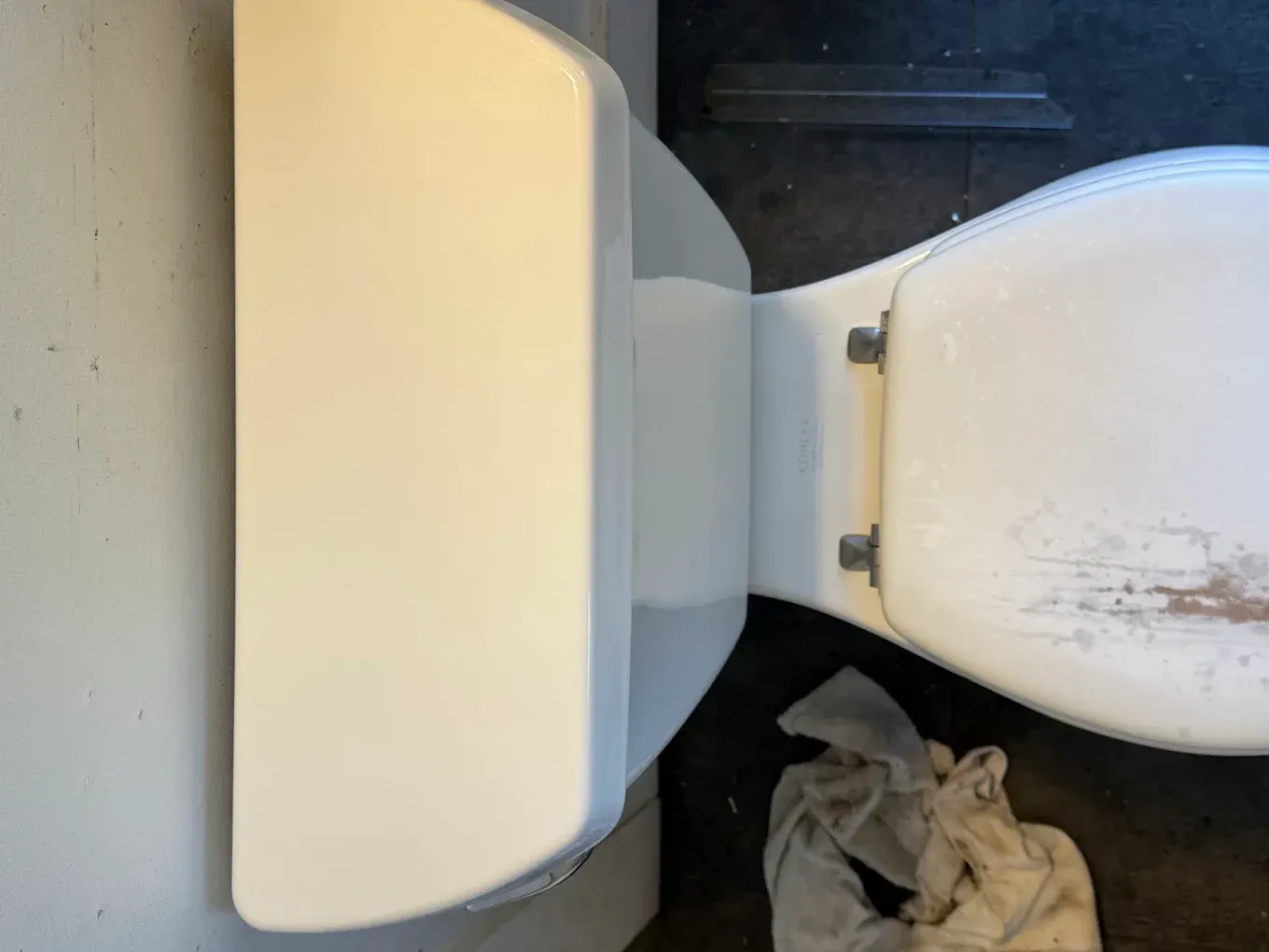 A toilet with a white tank and seat in a bathroom, with a trash bag on the floor beside it.