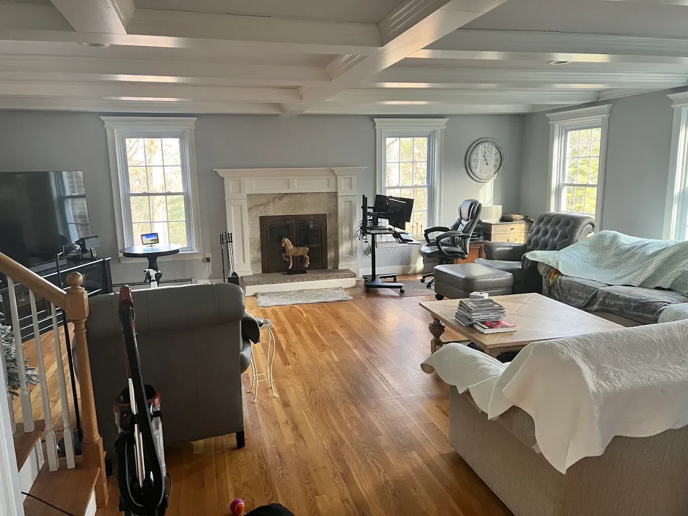 Bright living room with gray sofa, white fireplace, wooden floors, and large windows
