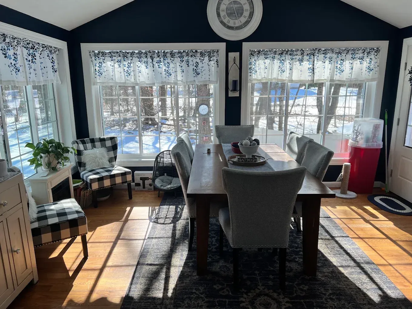 Bright sunroom dining area with a table, chairs, plants, and large windows overlooking a snowy yard