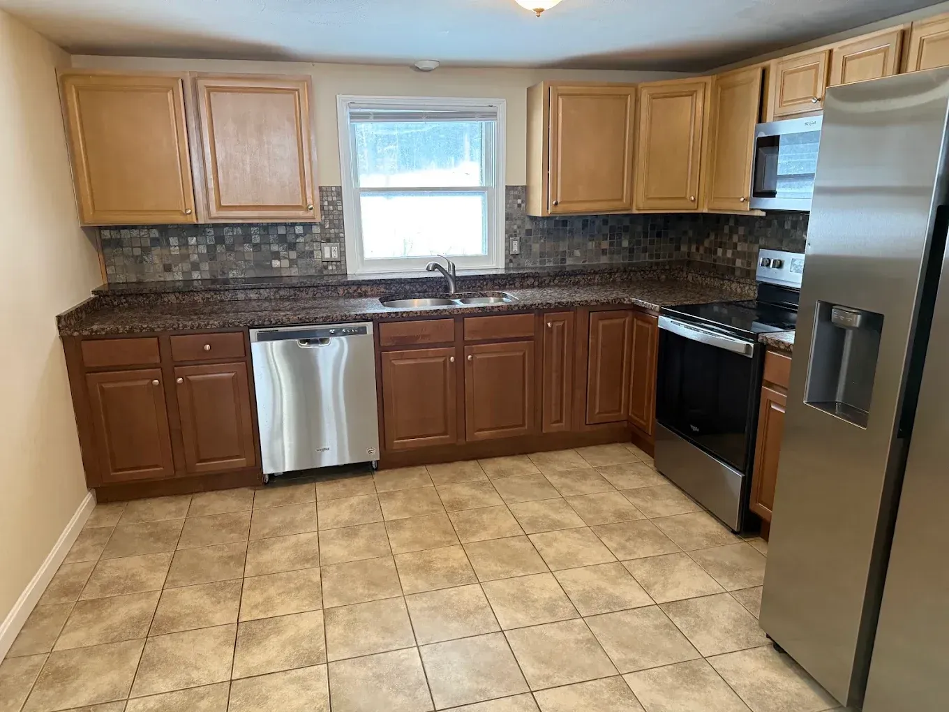 Small kitchen with wood cabinets, black countertops, stainless appliances, and a tiled floor.