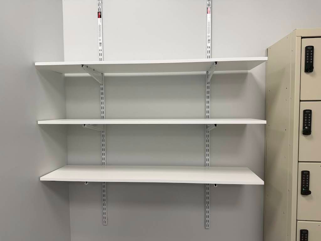 Empty white shelves mounted in a gray room beside beige lockers