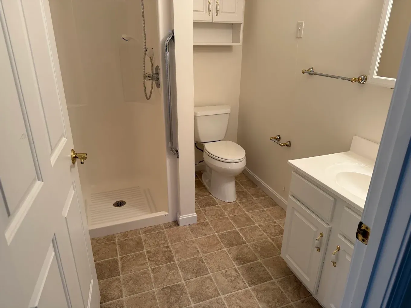 Accessible bathroom with walk-in shower, toilet, and vanity in beige and white.