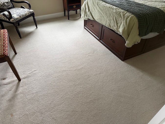 Bedroom with beige carpet, bed with green-striped bedding, and two chairs near a window.