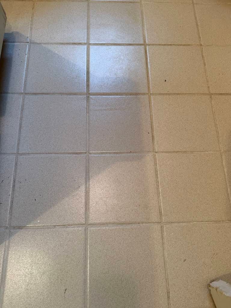 Beige tiled floor with sunlight reflections and a dark shadow along the left edge