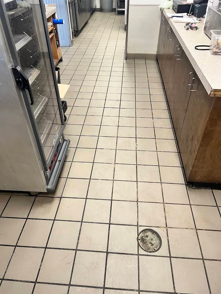 Kitchen aisle with white tile floor, stainless fridge on left, counter on right, and a floor drain ahead