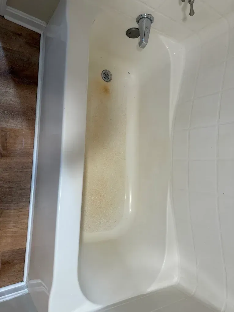 A white bathtub with a showerhead and stained, worn interior next to white tile walls.
