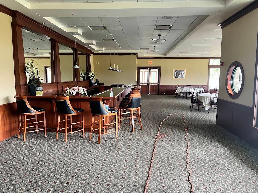 Empty restaurant lounge with bar stools, tables, patterned carpet, and a large wall clock