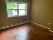 Empty room with brown hardwood floor, beige walls, and a window letting in green outdoor light