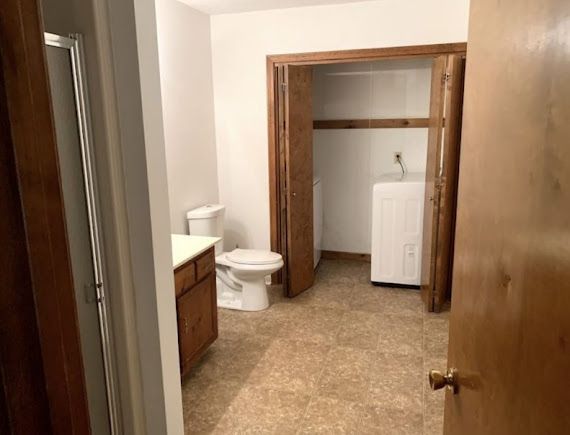 Bathroom with beige tile, wood trim, toilet, vanity, and white washing machine in adjoining room.