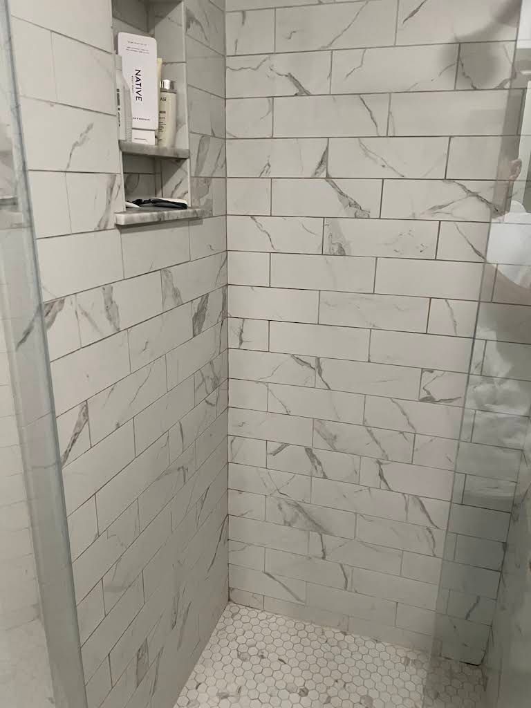 Tiled shower stall with built-in soap dispenser and textured white floor tiles