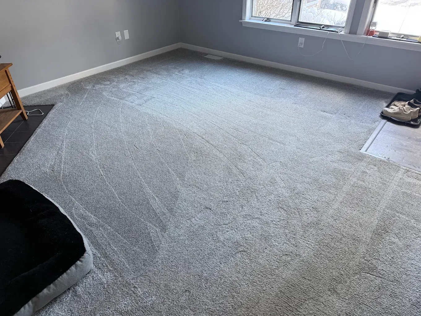 Empty gray-carpeted room with light gray walls, windows, and a small chair in the corner.