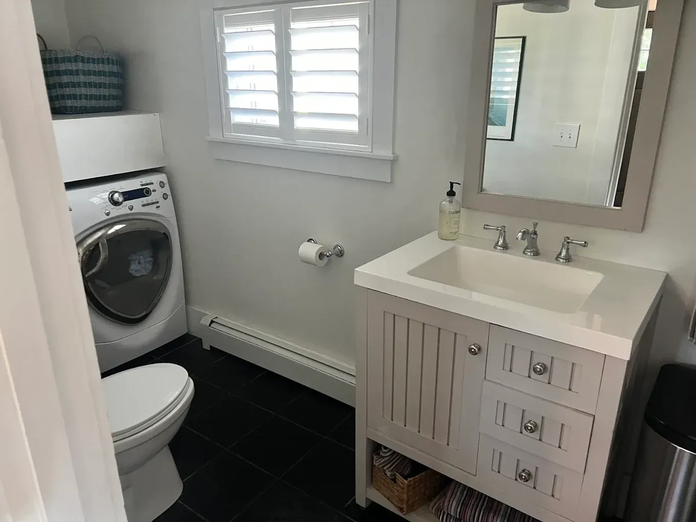 Small bathroom with toilet, washer, sink vanity, mirror, and black tile floor.