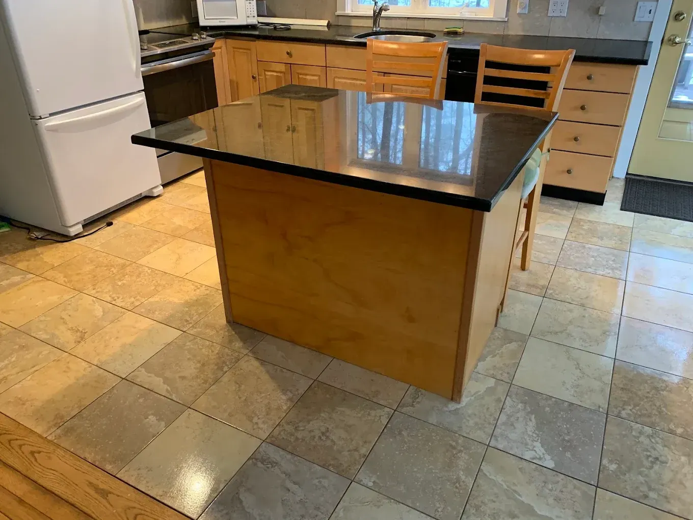 Kitchen island with dark granite top and wooden base in a tiled kitchen