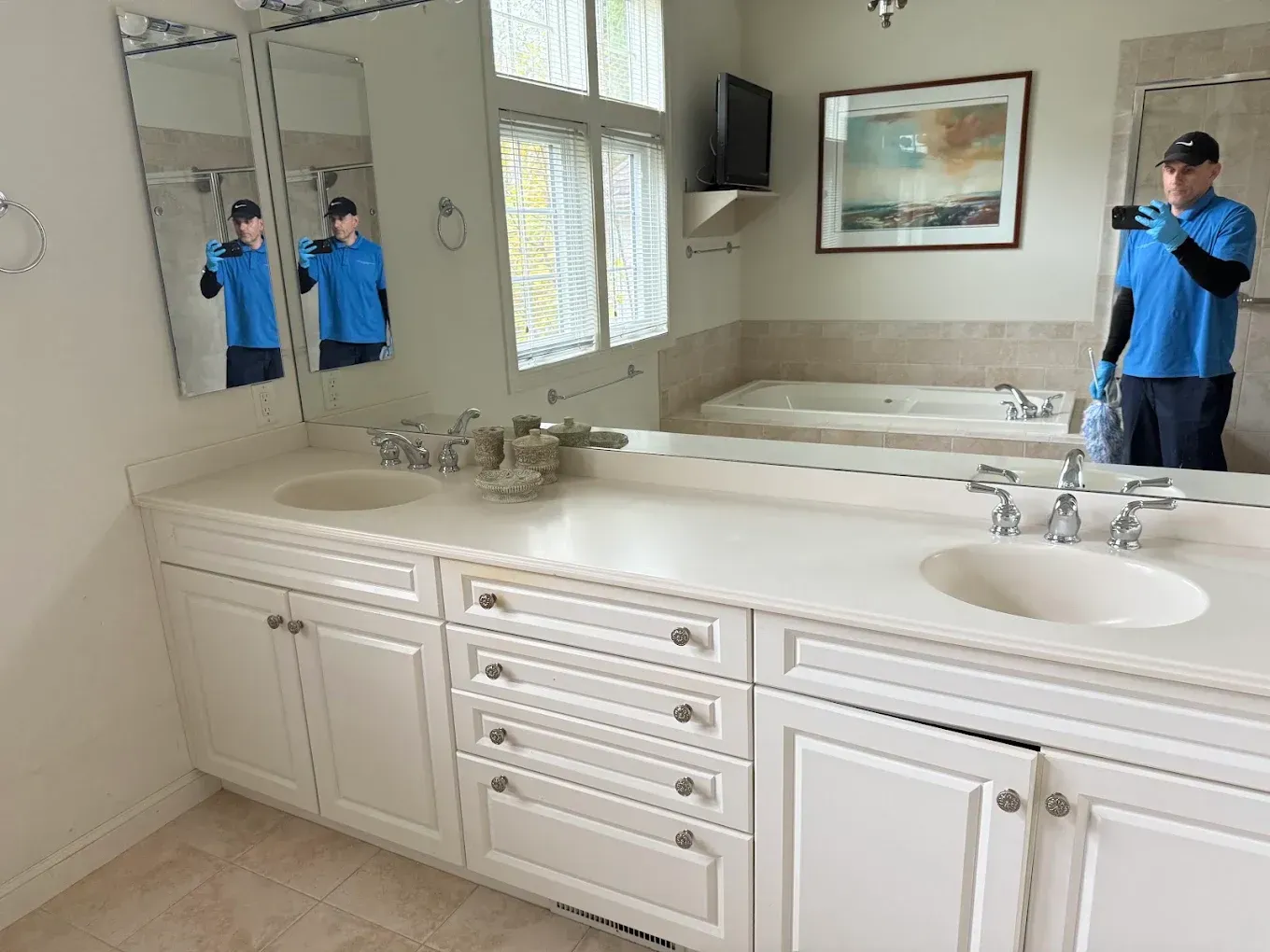 Bright bathroom with double sinks, large mirror, and blue-clad person reflected at the right sink.