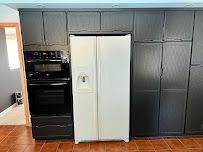 Modern kitchen wall with black built-in oven, white fridge, and dark gray cabinets on wood floor