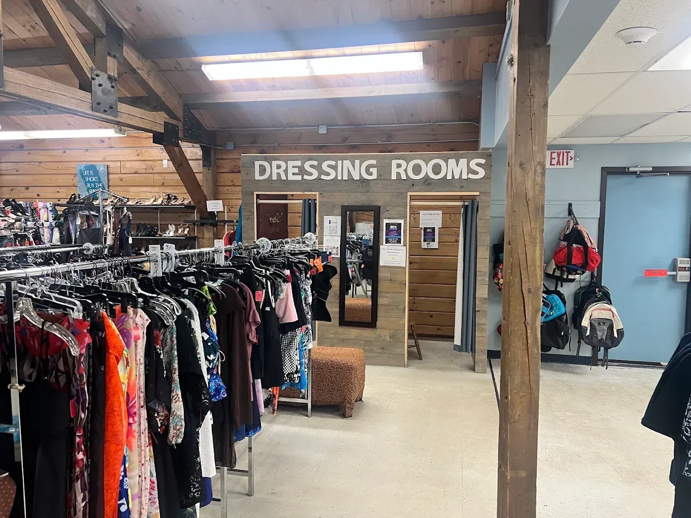 Clothing store with racks of dresses and a wooden dressing room area in the background.