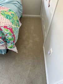 Bedroom floor beside a bed with a colorful quilt and a white dresser, showing a beige carpet runner.