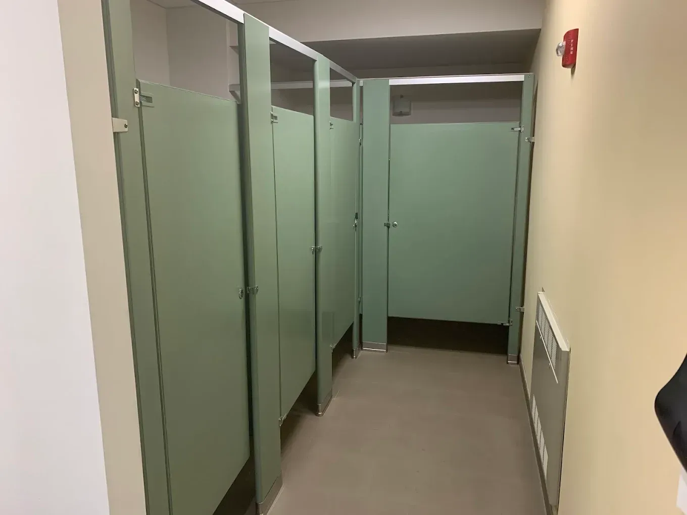 Public restroom hallway with green stall doors and beige walls