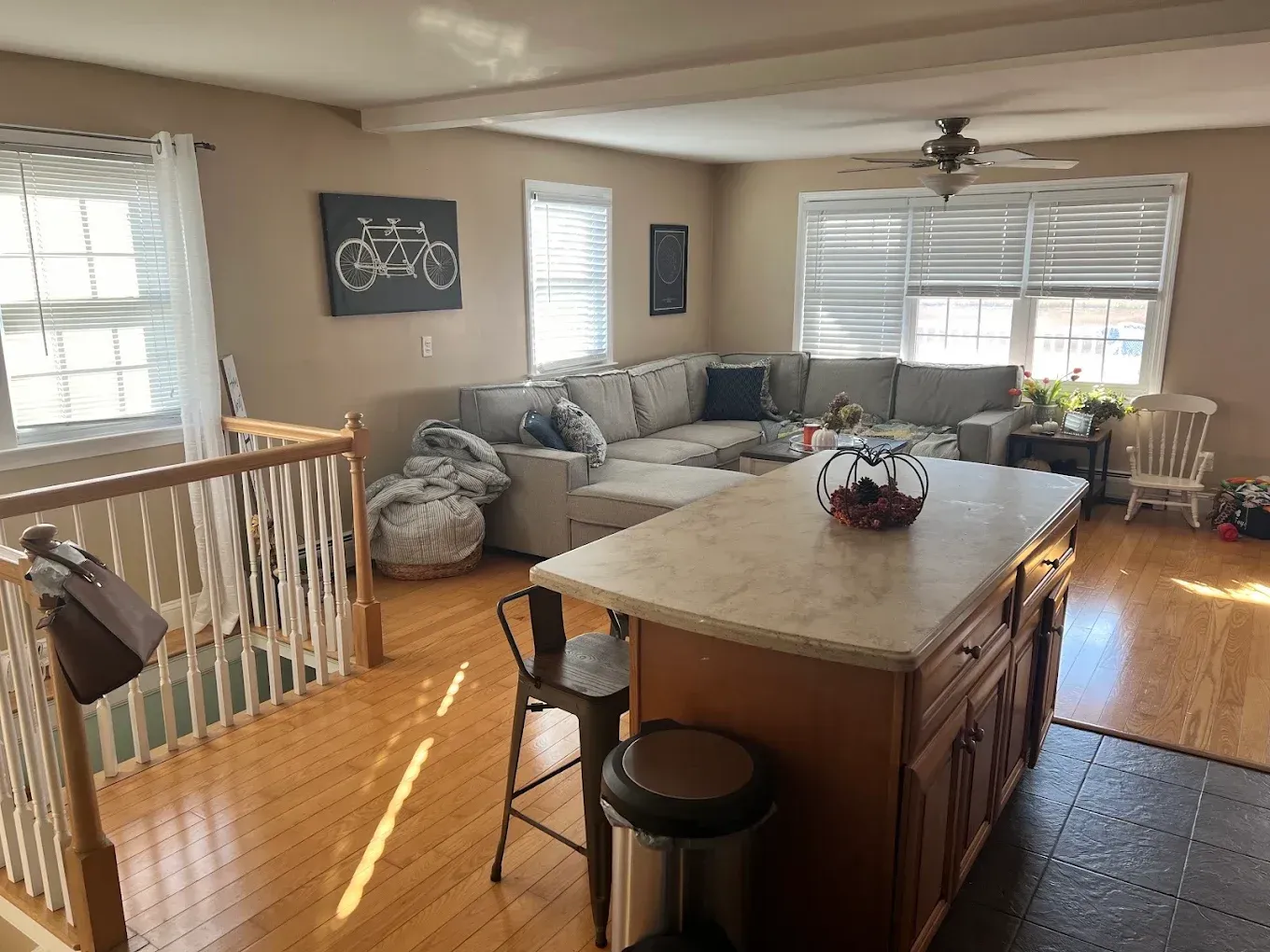 Bright living room with gray sectional, wooden island, and sunlight streaming through large windows.