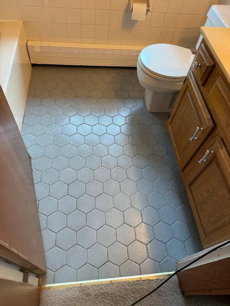 Small bathroom with hex tile floor, toilet, and wooden vanity cabinet.