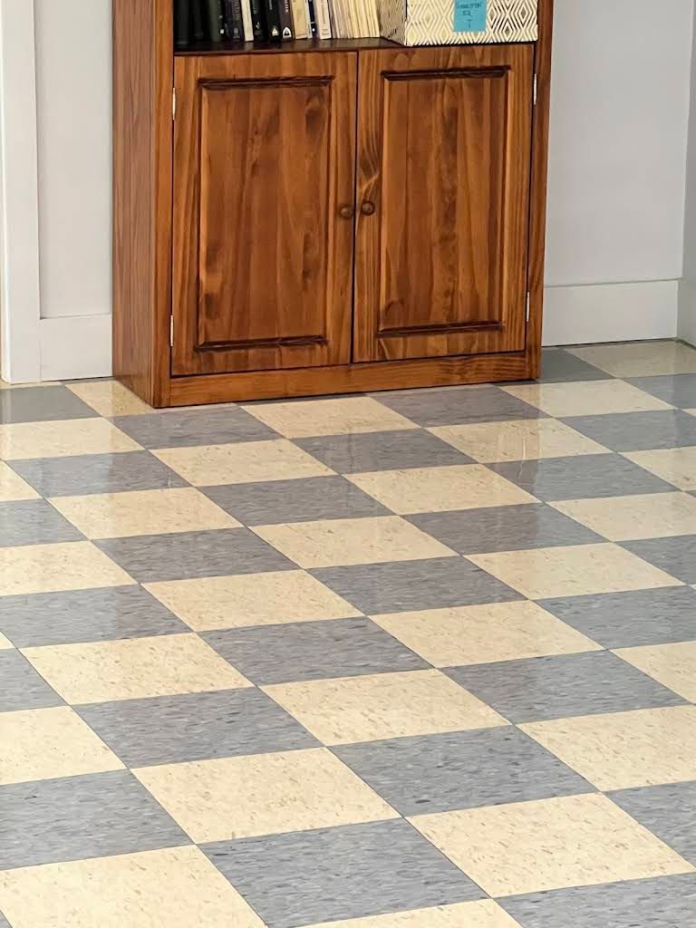 Checkered tile floor beside a wooden cabinet against a white wall