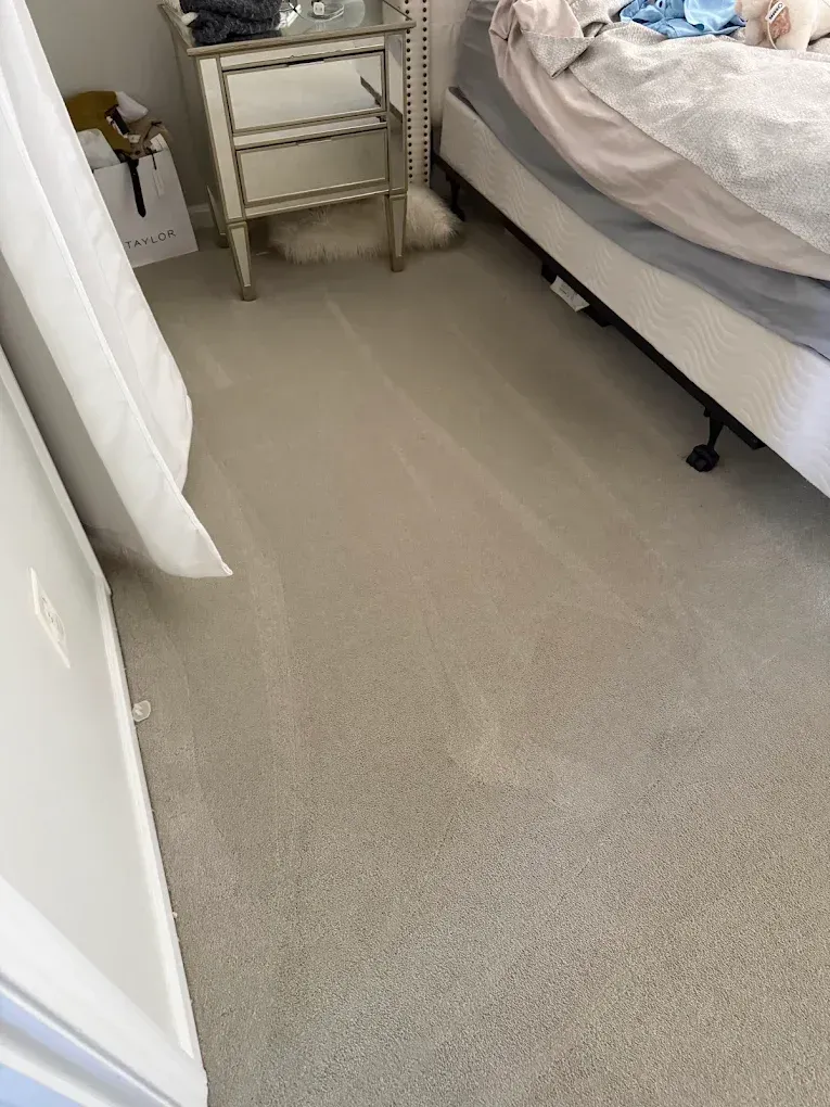 Small bedroom with bed, beige carpet, and a narrow bedside table near a curtain.