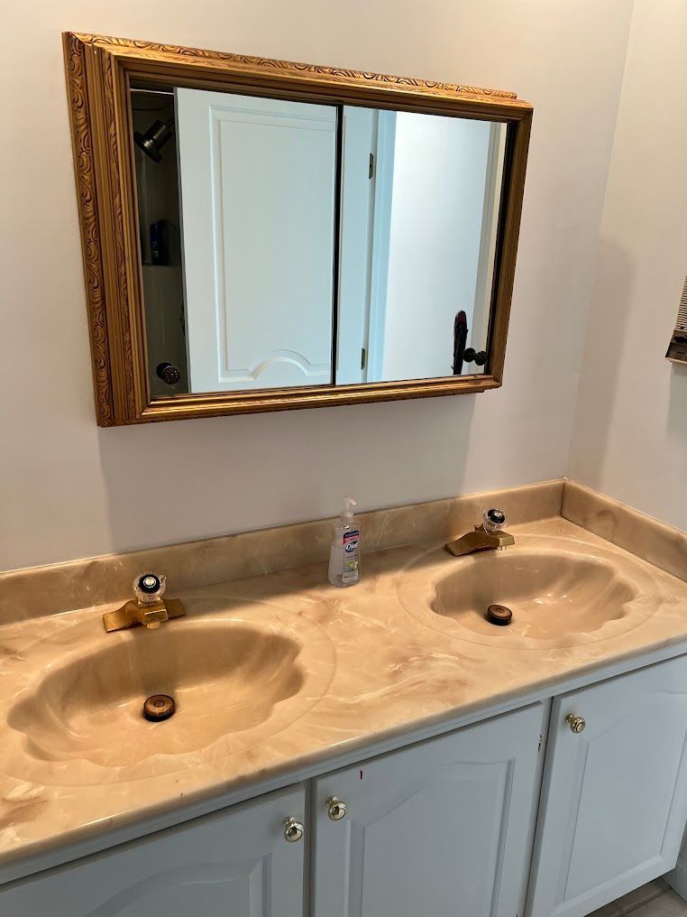 Bathroom vanity with double sinks, beige countertop, and a gold-framed mirror above blue cabinets.