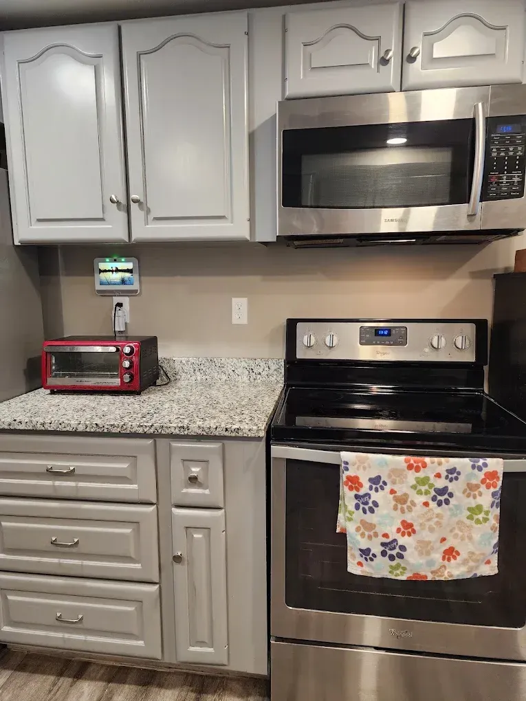Kitchen with white cabinets, stainless steel microwave and stove, and a red toaster oven on the counter.