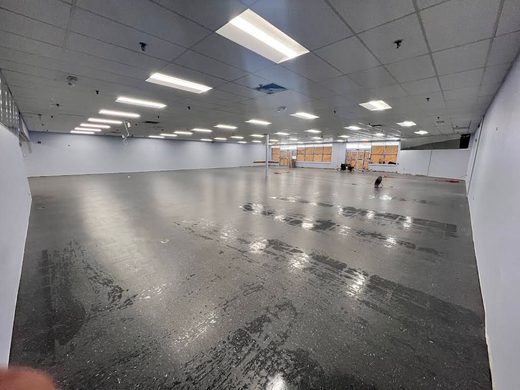 Large empty indoor hall with glossy gray floor, white ceiling lights, and tables against the far wall