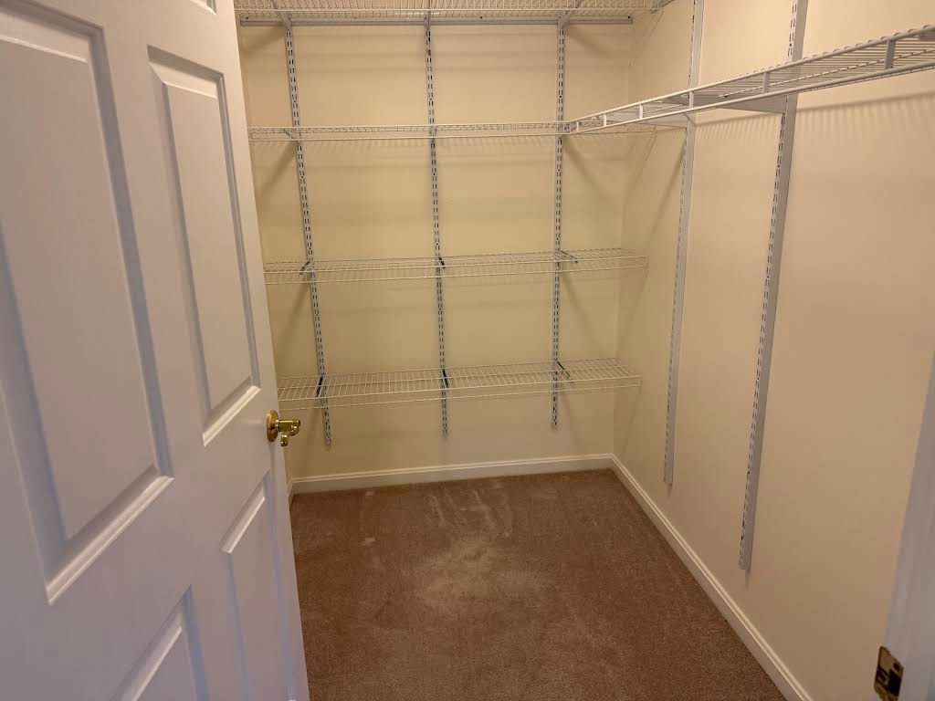 Empty walk-in closet with white wire shelving, beige walls, and carpeted floor