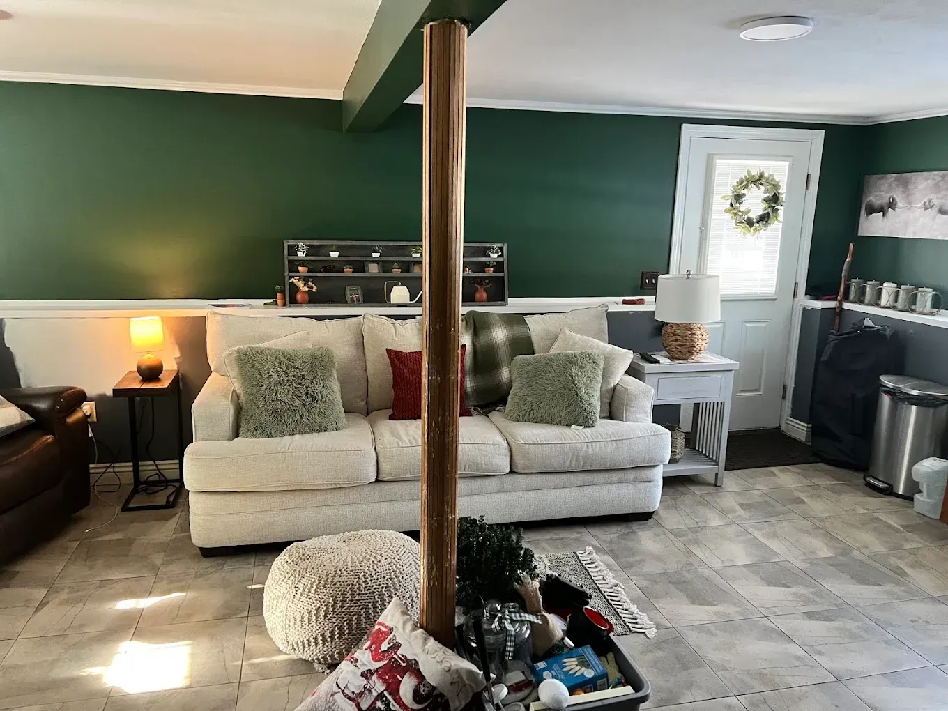 Cozy living room with beige sofa, dark green walls, lamp, and tiled floor; wooden post in foreground