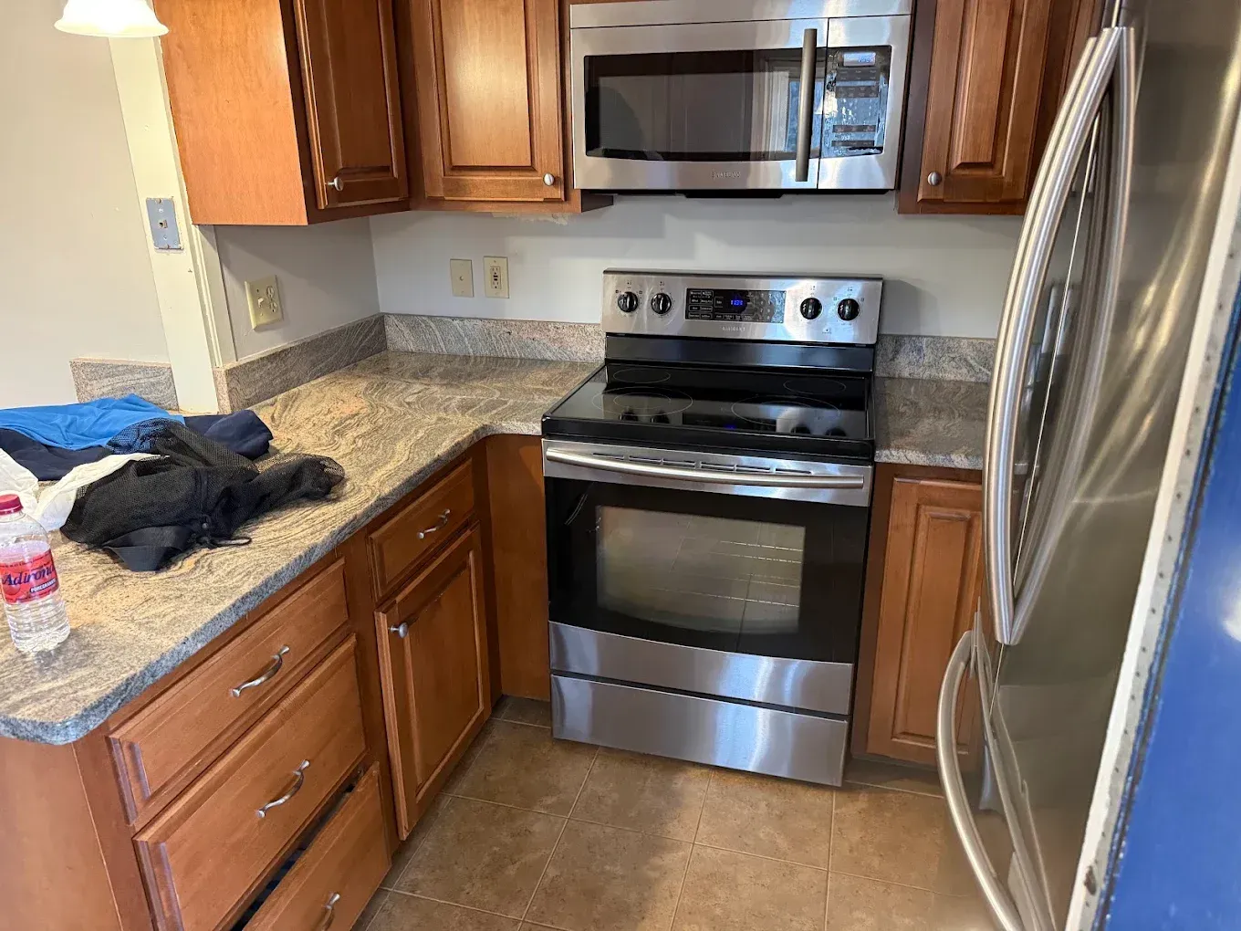 Compact kitchen with stainless steel stove and refrigerator, wood cabinets, and granite countertops.
