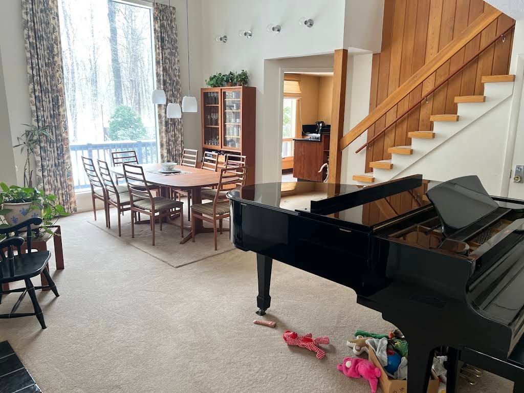 Living room with a black grand piano, dining table, staircase, and large window with curtains