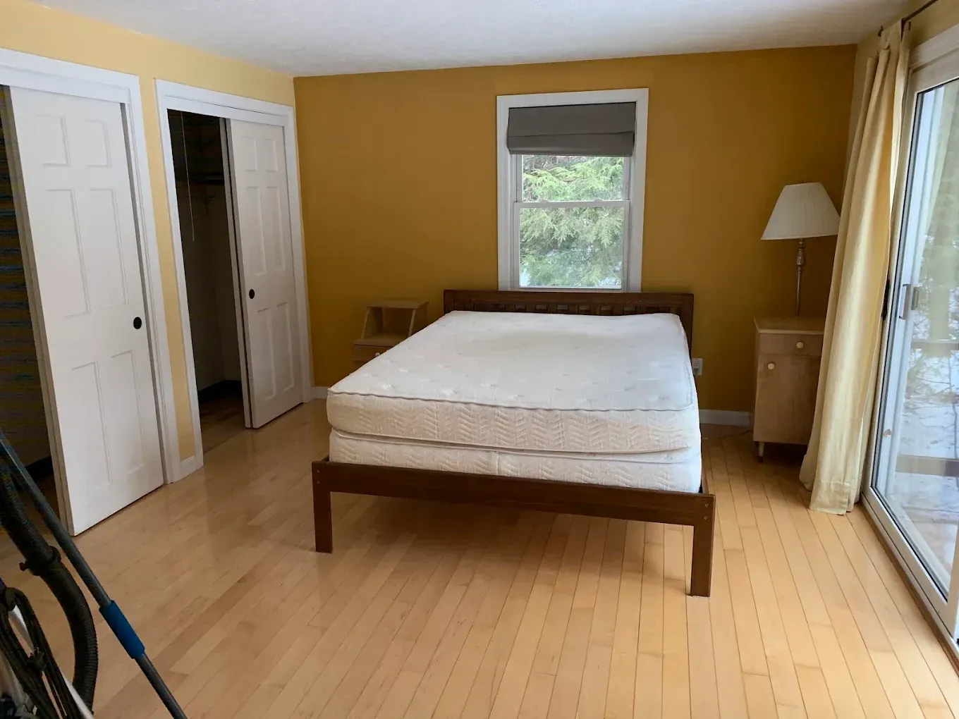 Bedroom with a wooden bed, beige walls, white closet doors, and a window with blinds.