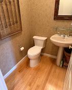 Small beige bathroom with a toilet, sink, wood floor, and window blinds.