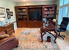 Home office with dark wood built-in shelves, desk, leather chair, and a patterned rug by a window