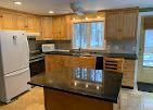 Kitchen with wooden cabinets, white appliances, and a black granite island under a window.