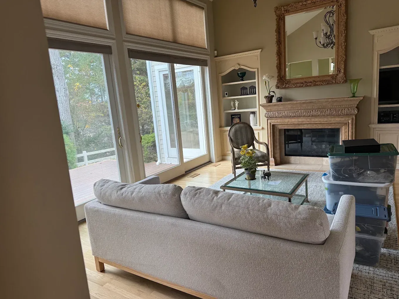 Bright living room with a gray sofa, fireplace, large windows, and a glass coffee table.