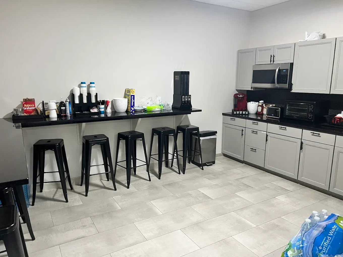 Kitchen with black countertop, stools, white cabinets, microwave, and tiled floor