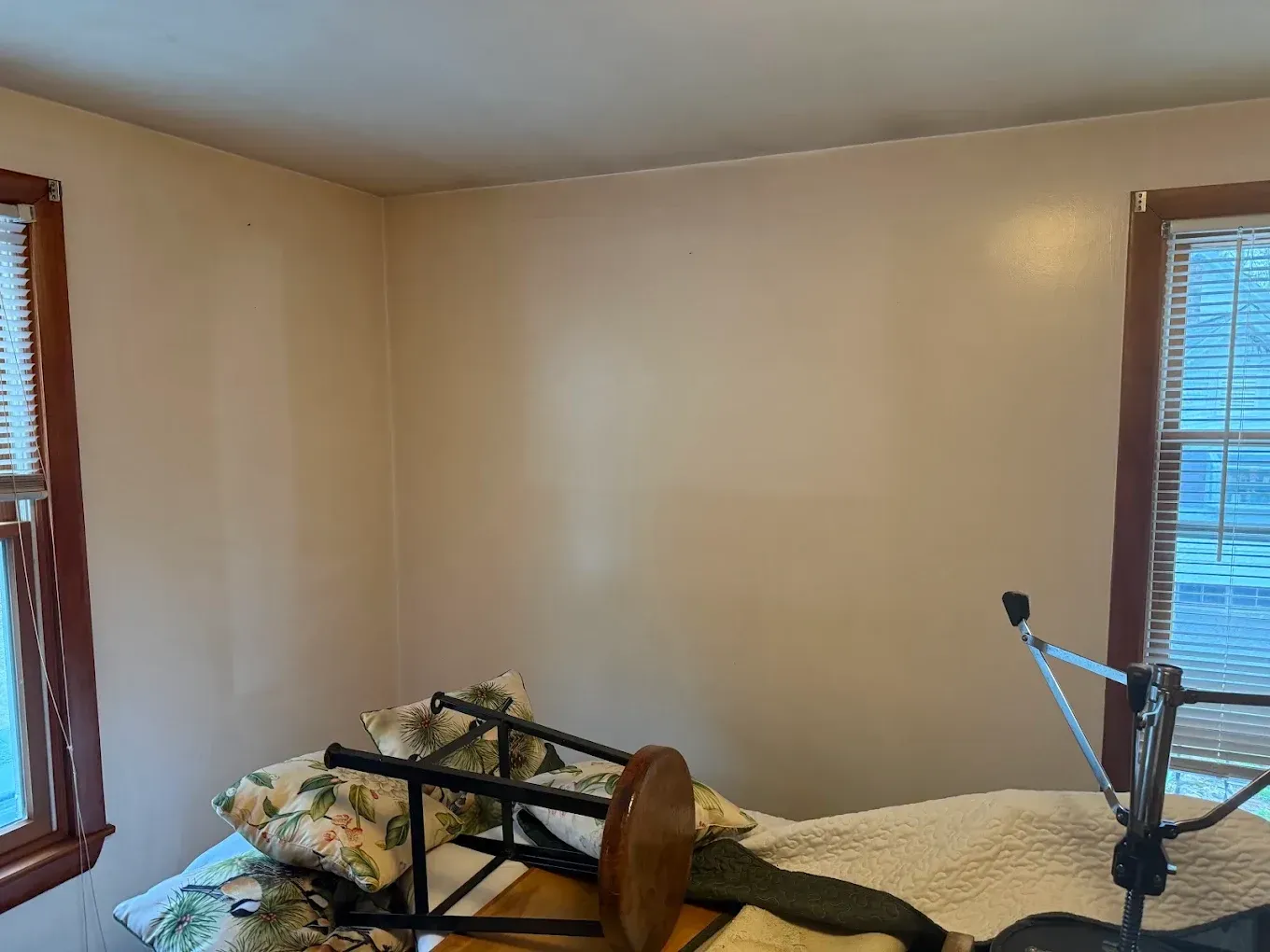 Small beige bedroom with a bed, floral bedding, and windows on two walls.