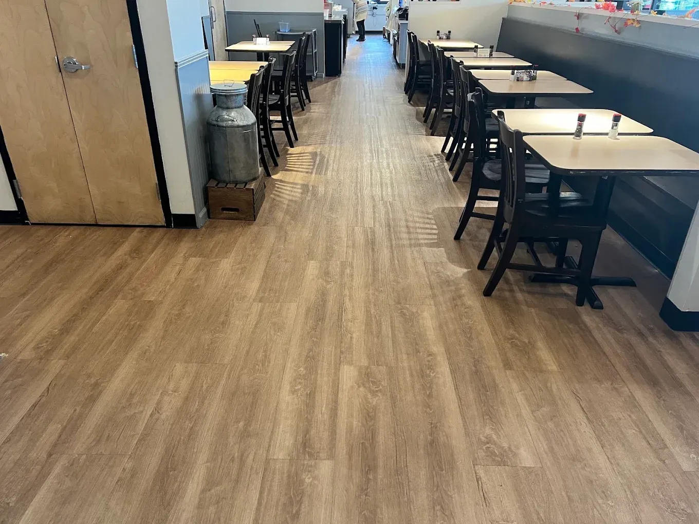 Empty cafeteria with wooden floors, rows of tables and chairs, and a hallway in the distance