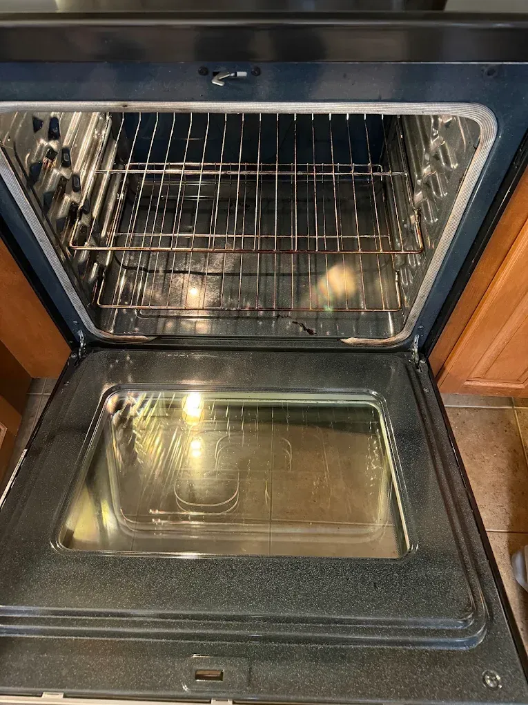 Open oven with racks and a baking tray inside, oven light on.