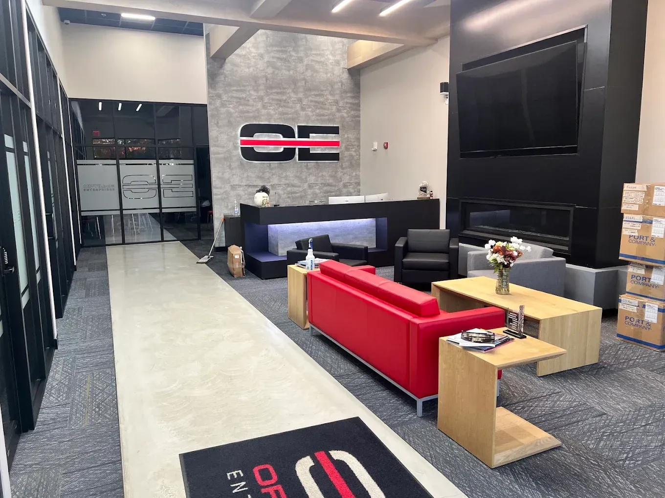 Modern office lounge with red sofa, black chairs, TV, and reception desk in a sleek interior