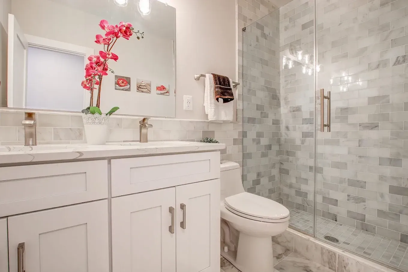 Bright white bathroom with vanity, mirror, pink orchid, and glass-enclosed shower