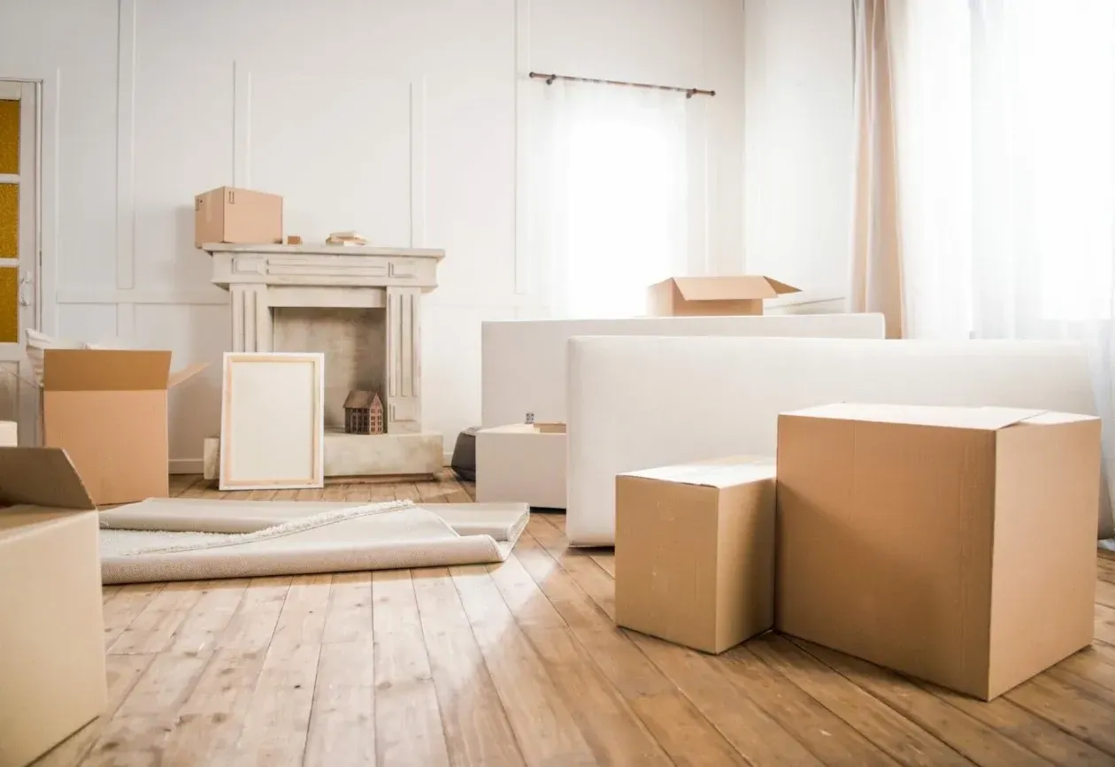 Bright living room with moving boxes, a rolled rug, and white furniture in soft daylight