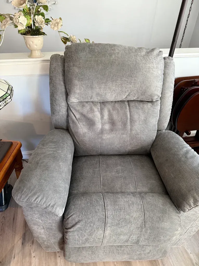 Gray upholstered recliner chair in a living room beside a side table and decorative flowers