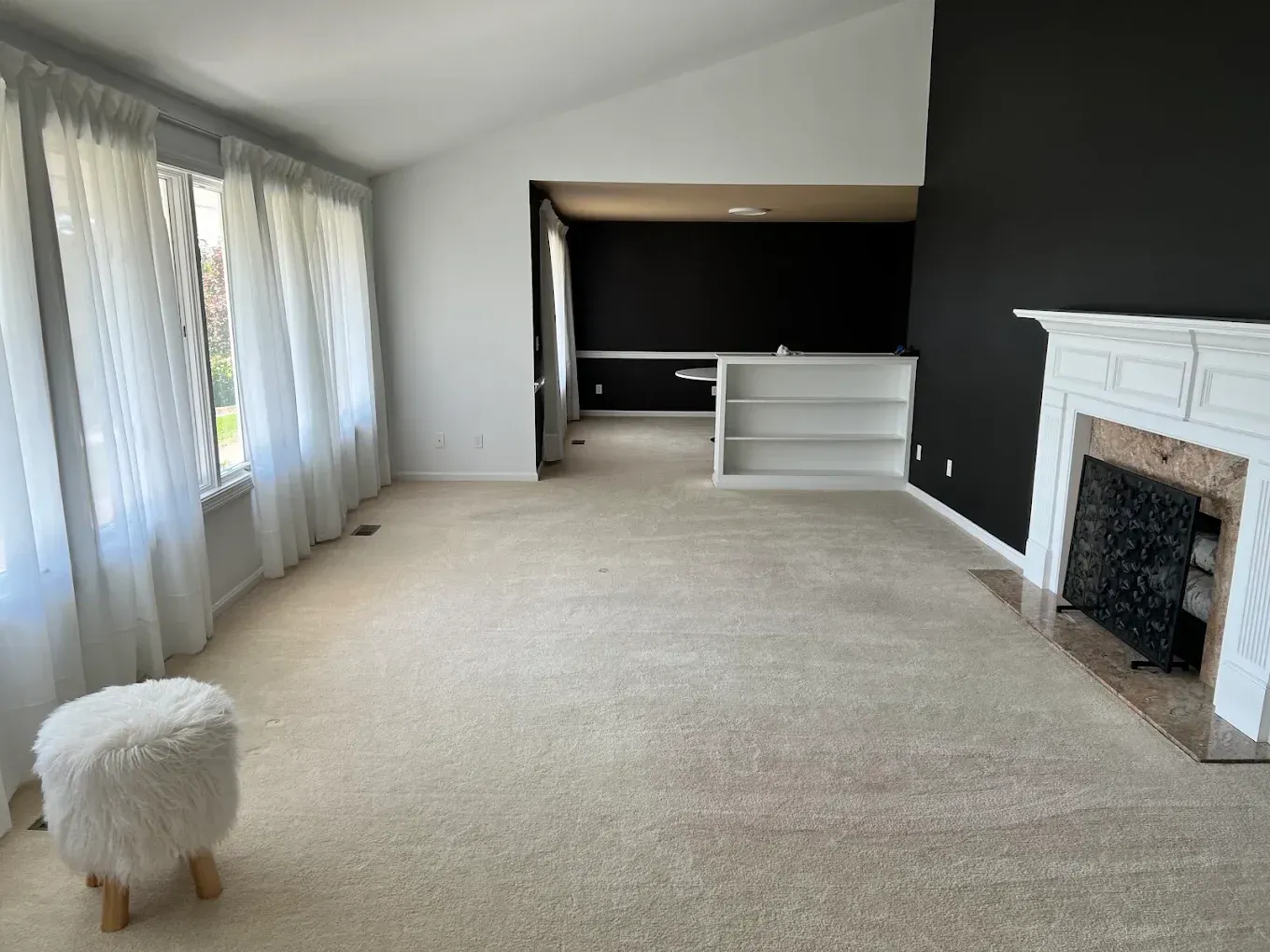 Empty living room with beige carpet, dark accent wall, fireplace, and large curtained windows