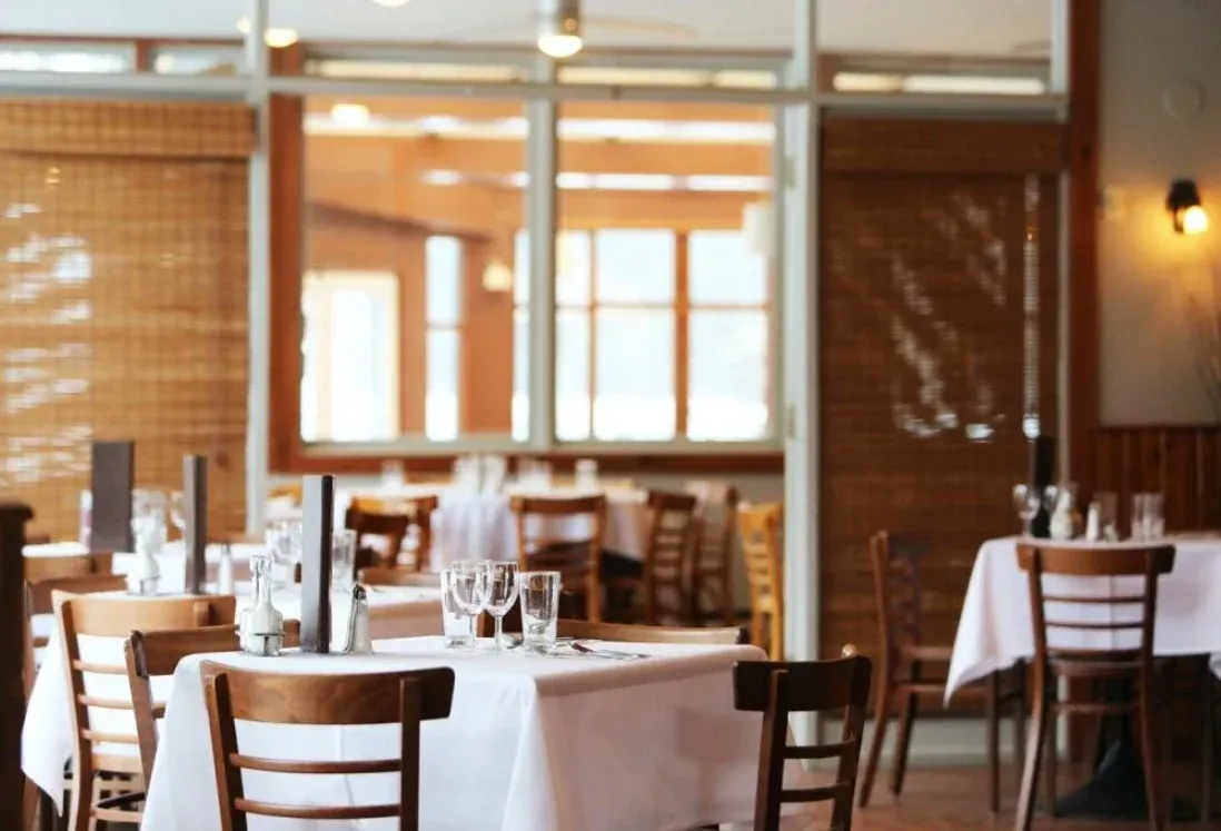 Empty restaurant dining room with tables set in white tablecloths and wooden chairs
