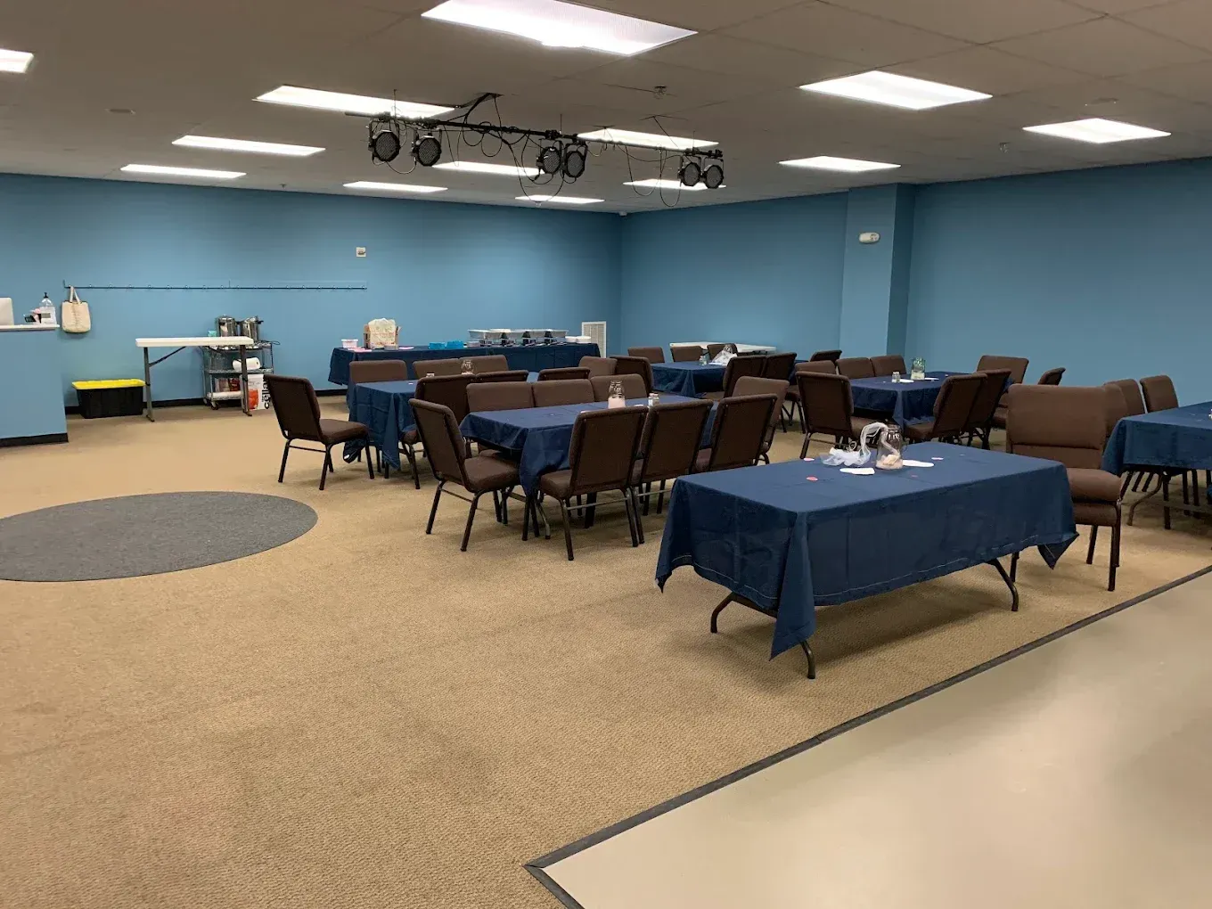 Blue-walled meeting room with round tables, chairs, and a projector setup